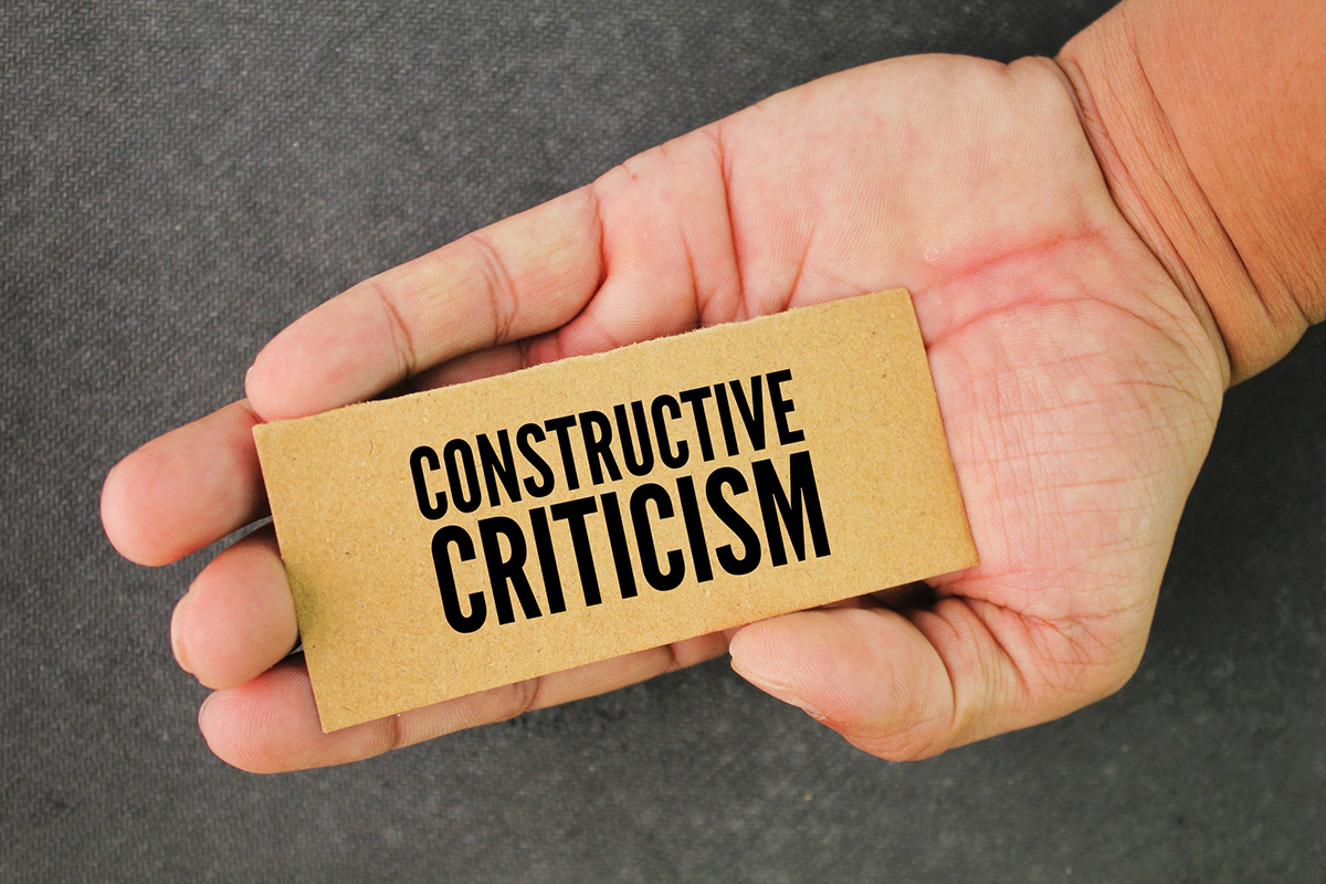 Hand holding a paper with the words “Constructive Criticism,” highlighting positive feedback and growth in team settings.