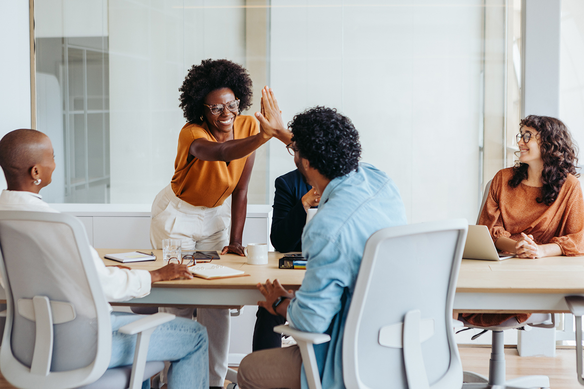 Diverse business team high-fiving in boardroom, showing teamwork, collaboration, and project success.