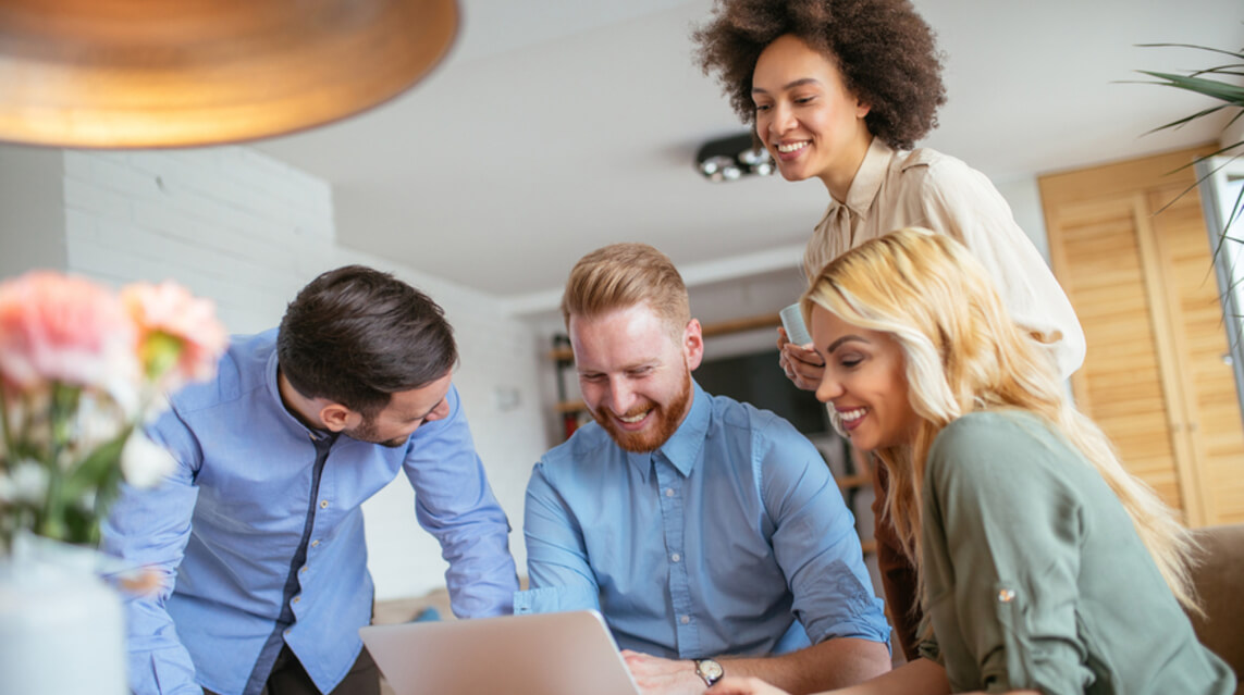 Four smiling nonprofit staff members look at a laptop in their office.