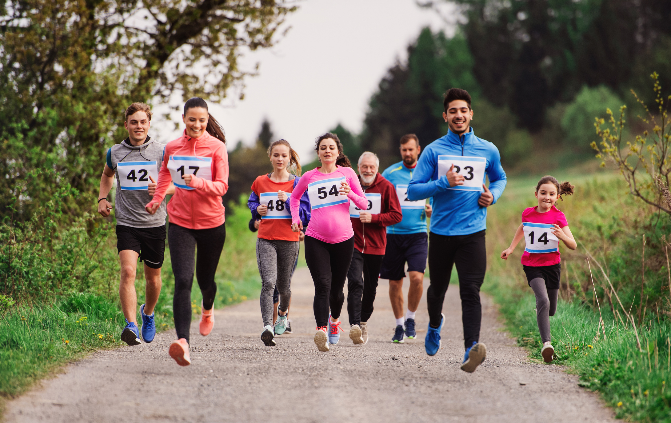 Children and adults run in a fun run, wearing numbered bibs.