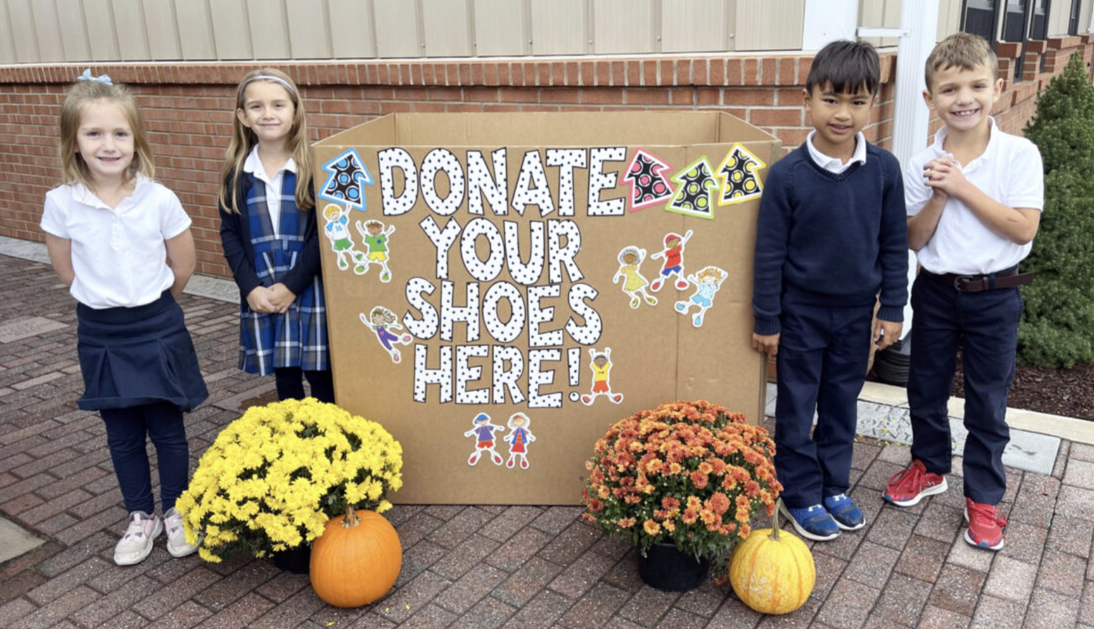 Children stand beside a shoe donation box for their school’s shoe drive fundraiser.