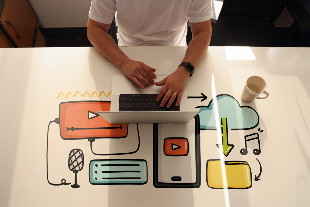 Person working on laptop with illustrated icons of video, cloud storage, music, and mobile apps representing social media content creation and digital marketing strategy.