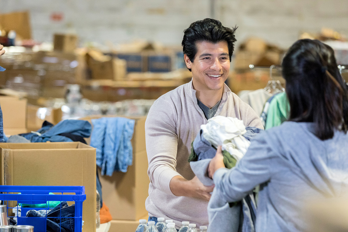A woman handing clothes to a man for donation.