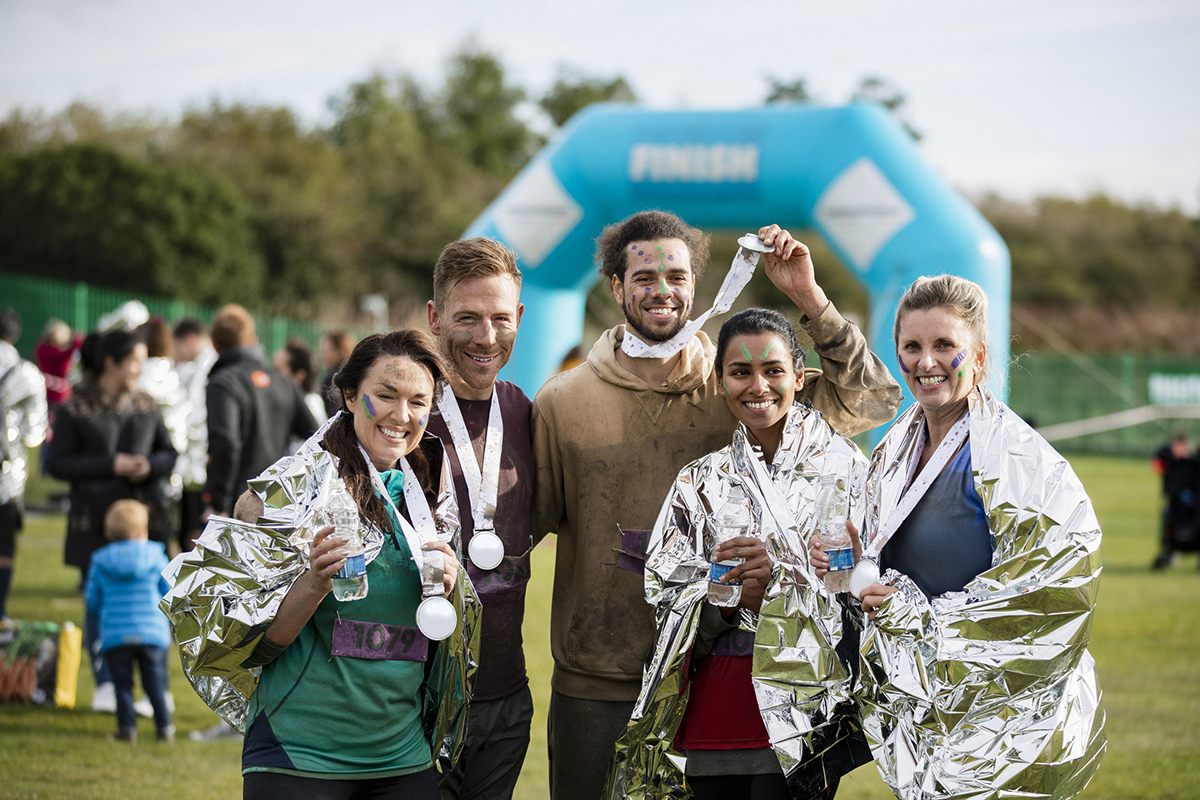 Group of friends smiling and holding medals after completing a charity 5K fundraiser, celebrating their community impact through fitness and giving back.