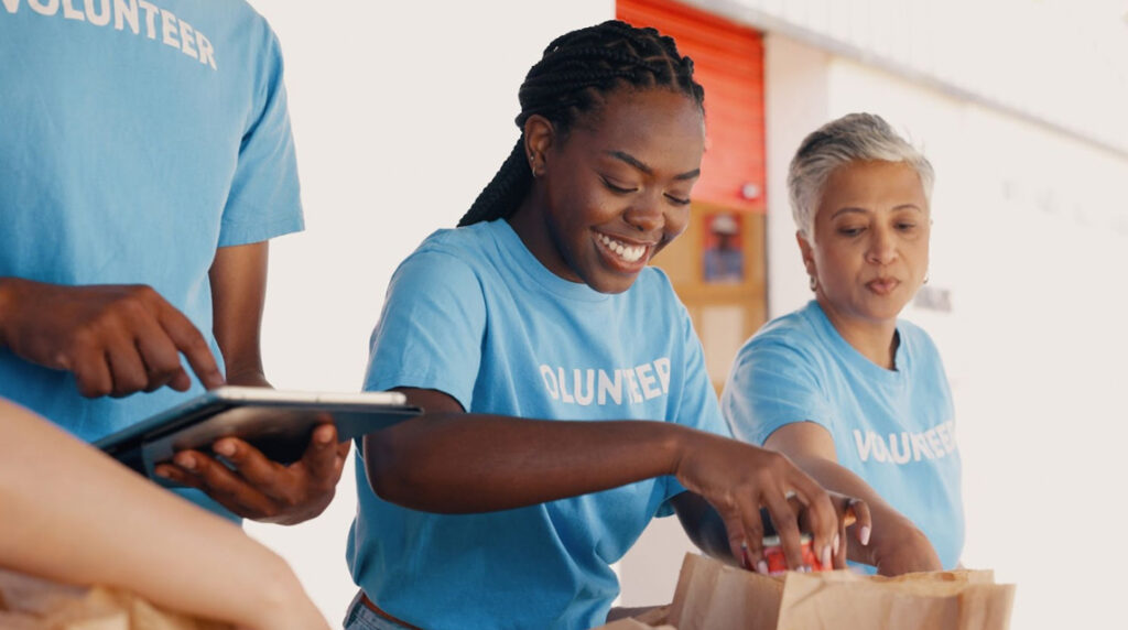 A group of volunteers in blue t-shirts packing food in paper bags.