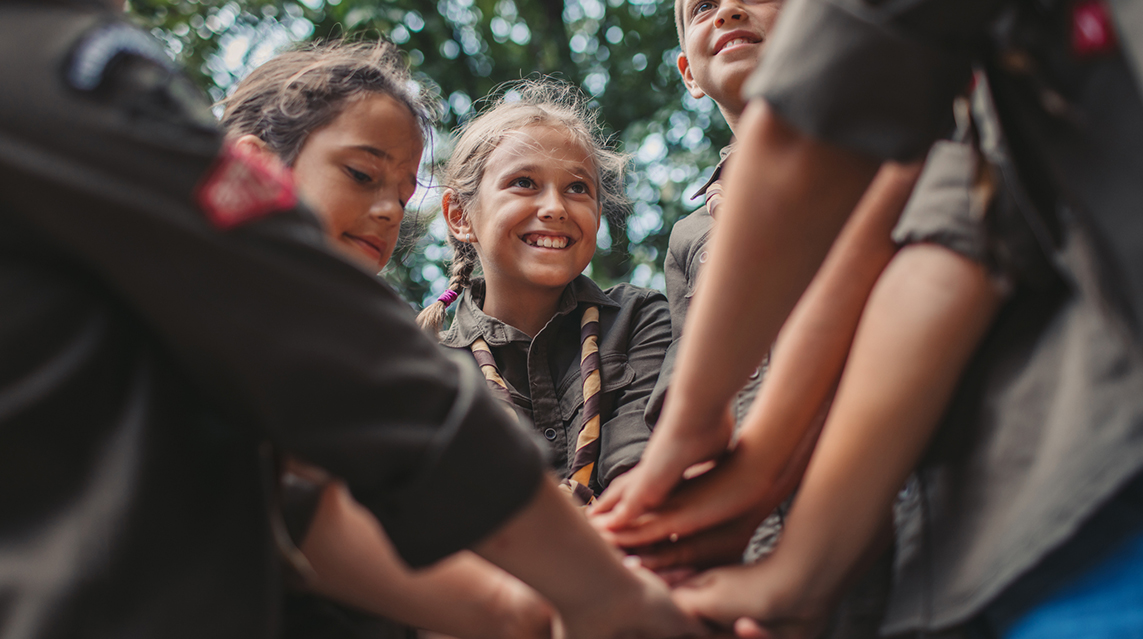 Group of young scouts joining hands together, showing their unity.
