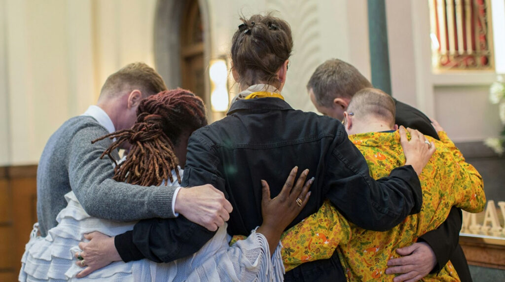 A group of people standing with their arms around each other at a funeral in a church.