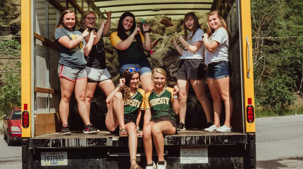 A group of cheerleaders posing the back of a Funds2Ougs collection truck with their shoe collection.