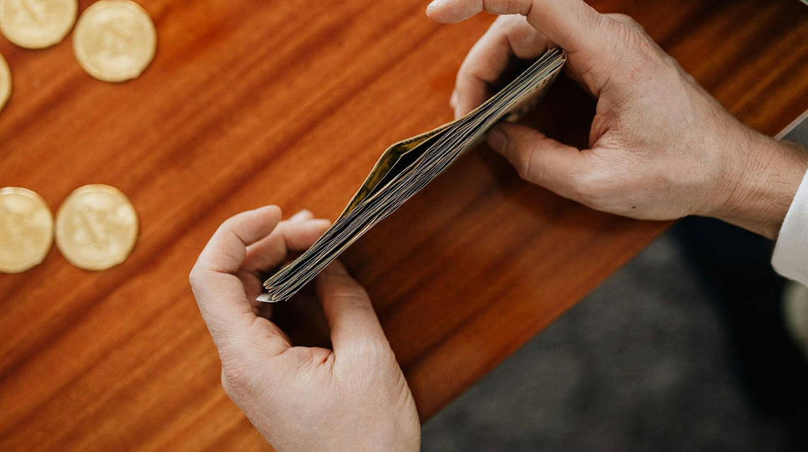 A person holding a stack of money at a desk with coins in the background.