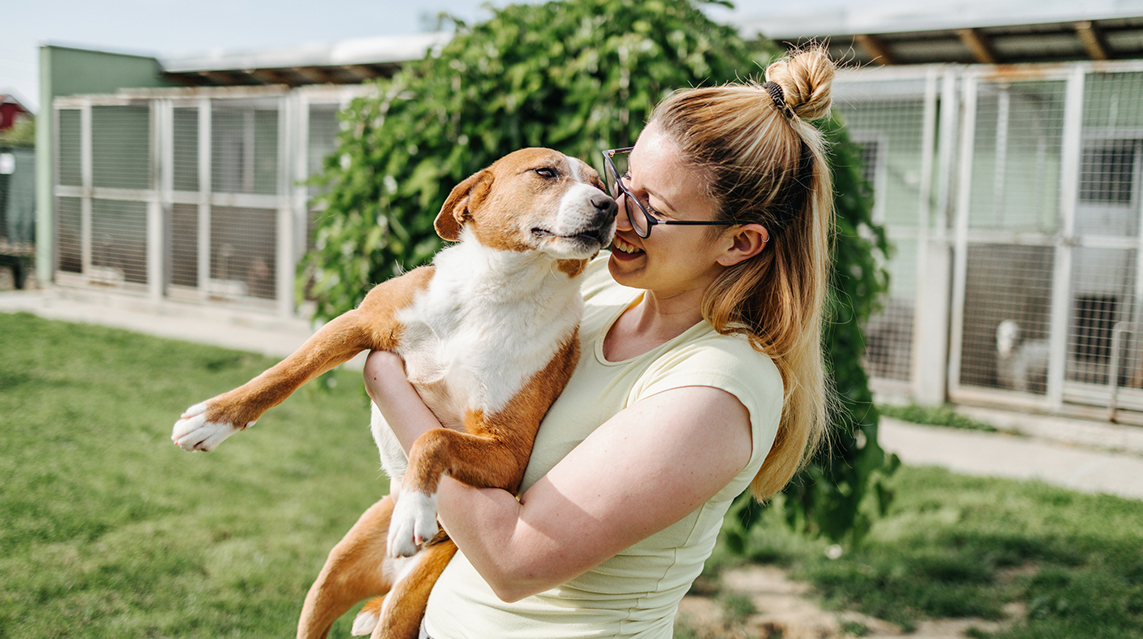A young woman lifts a dog and hugs it while smiling and nuzzling its face