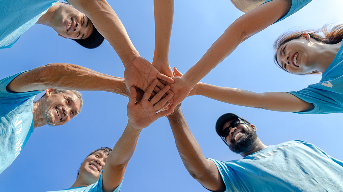 A group of people wearing blue shirts putting their hands together.