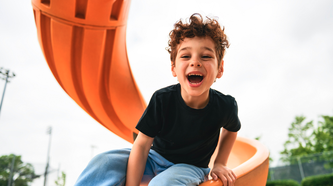 A child photographed smiling while playing on the slide at a playground.
