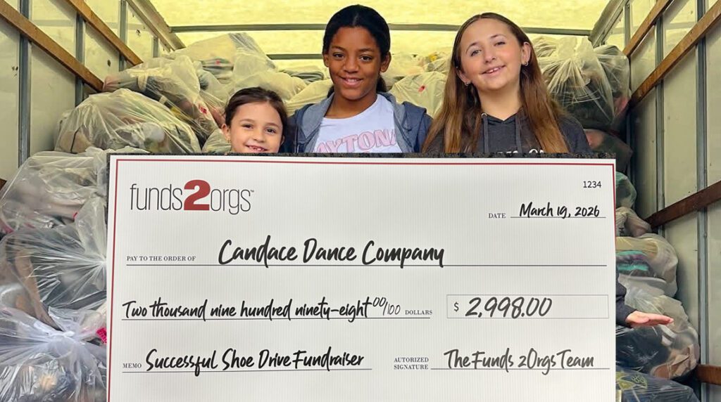 Three children celebrate a nonprofit community engagement shoe drive fundraiser with bags of donated shoes and a $2,998 Funds2Orgs check.
