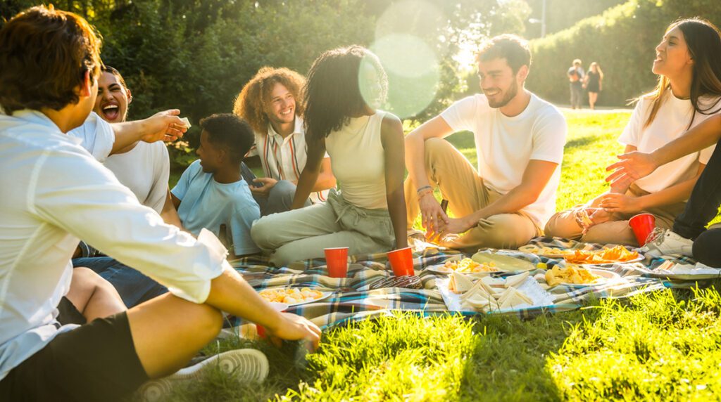 People laughing and sharing food at a sunny outdoor picnic, which is ideal for nonprofit summer fundraising and donor engagement events.