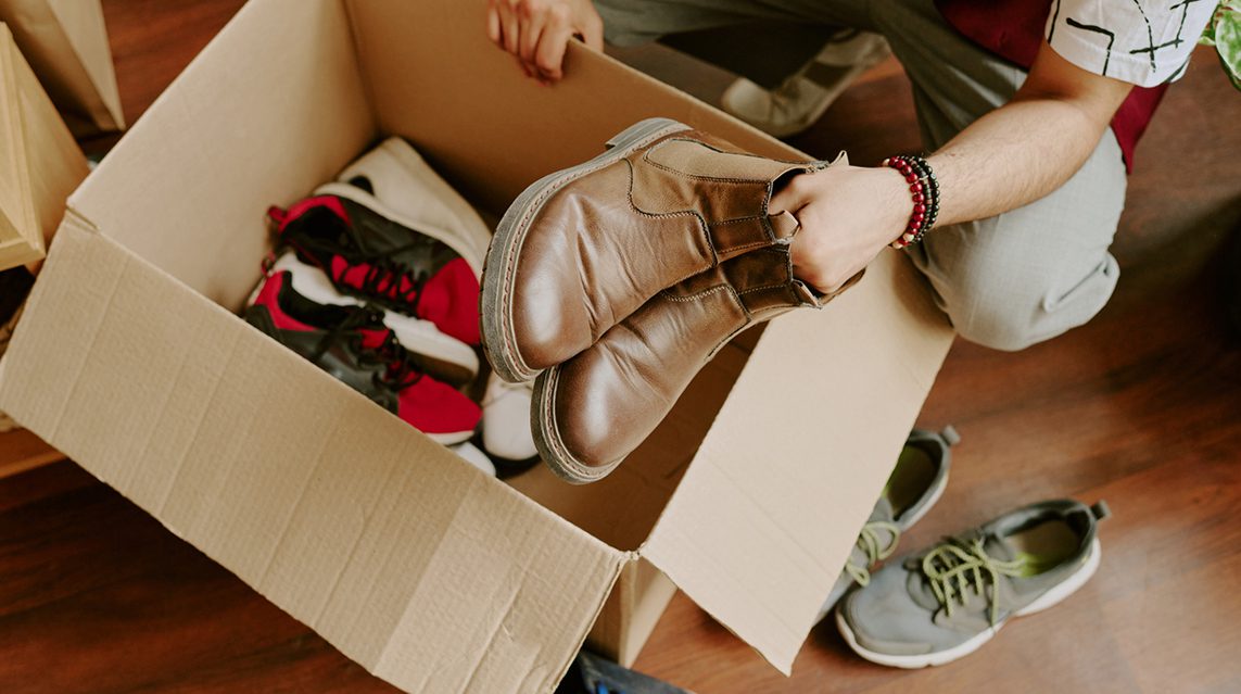 Someone places pairs of shoes, including boots and athletic shoes, into a cardboard box.