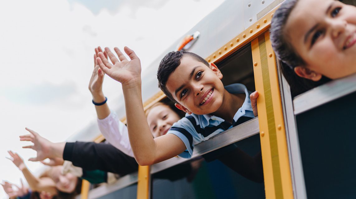A group of children wave goodbye as they head out on a field trip.