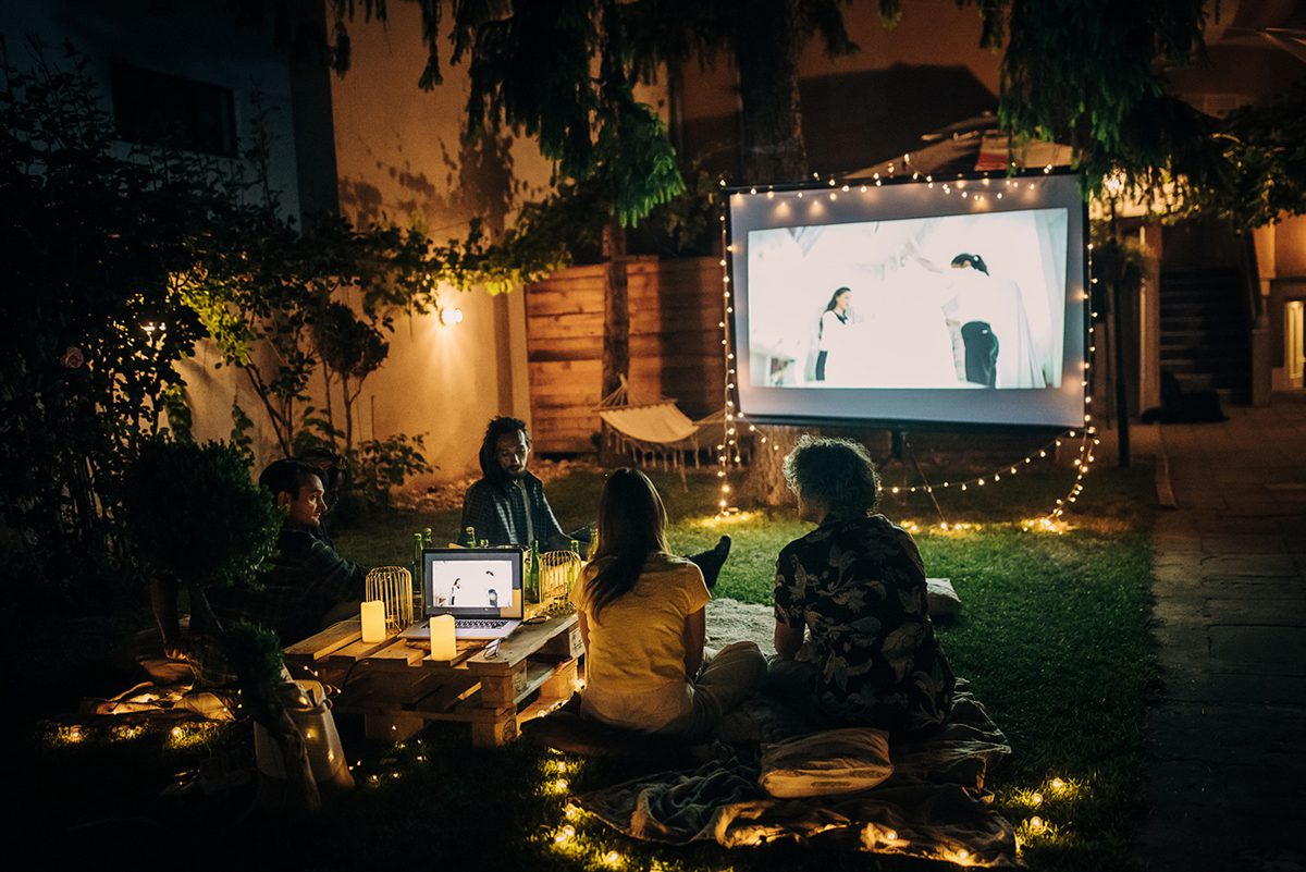 People watching a movie on a projector screen in a backyard garden at night after a silent auction.