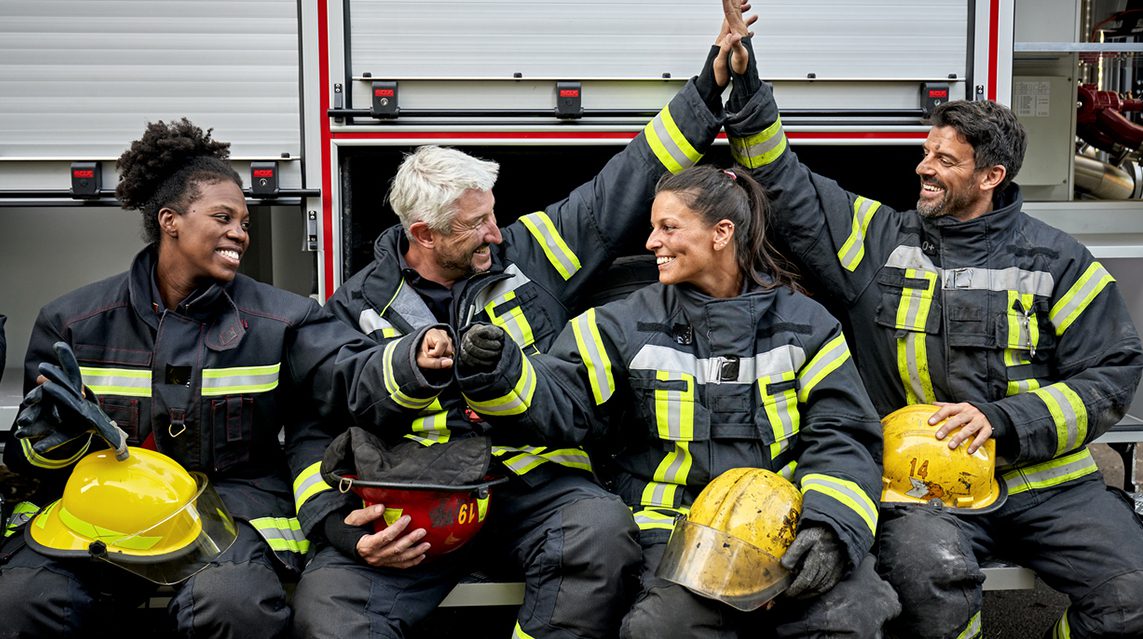 Diverse group of volunteer firefighters in gear smiling and supporting one another.